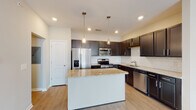 This single-floor residence offers a thoughtfully designed layout that balances functionality and modern style throughout. The kitchen serves as a focal point of the home, showcasing rich dark cabinetry, granite countertops, a classic white subway tile backsplash, and a full suite of stainless steel appliances including a refrigerator with ice maker, range, microwave, and dishwasher. A central island with a matching granite surface provides additional prep space and casual seating. Pendant lighting above the island adds a refined finishing touch. Light hardwood-style flooring flows throughout the main living areas, reflecting natural light and creating a bright, airy atmosphere. The open living area is generously proportioned and features a ceiling fan, neutral-toned walls, and easy access to the kitchen via a connecting hallway. Bedrooms are well-sized, with at least one featuring a large walk-in closet equipped with extensive wire shelving and carpeted flooring for comfort. The bathrooms are finished with granite-topped dark vanities, light hardwood-style flooring, tub-shower combinations with tiled surrounds, and brushed nickel fixtures and hardware throughout. The overall design presents a clean, contemporary aesthetic with consistent finishes across all rooms.