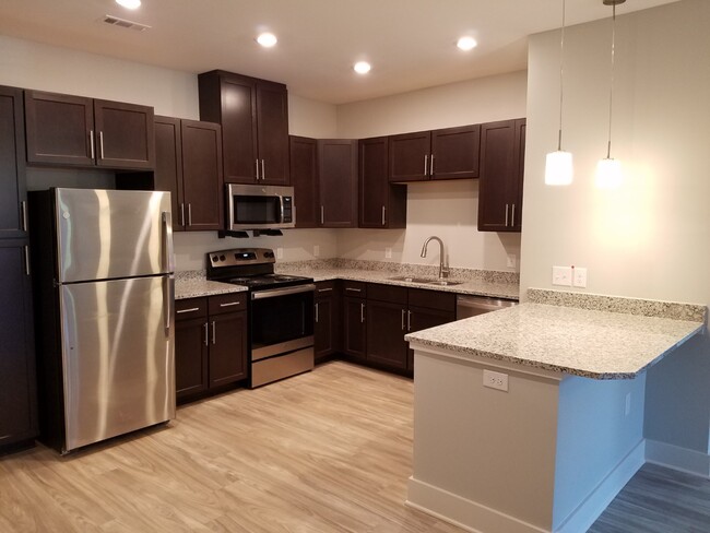 Beautiful kitchens with stainless steel appliances, granite countertops and wood-toned LVT - Evoke Living at Sugar Creek Apartments