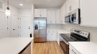 Located at 2405 Herrons Nest Pl NW in Concord, NC, this single-story, 2-bedroom, 2-bathroom home offers a clean, modern aesthetic with a thoughtfully designed layout. Warm hardwood-style flooring runs throughout the entire space, creating a cohesive and inviting atmosphere from room to room.

The kitchen is a standout feature, showcasing crisp white shaker-style cabinetry extending to the ceiling, sleek white countertops, a subtle tile backsplash, and a full suite of stainless steel appliances including a refrigerator with ice maker, range, and built-in microwave. A kitchen island provides additional prep and dining space, while the open connection to the living area promotes an easy flow for everyday living.

The living room is bright and open, illuminated by recessed lighting and a generous window that brings in natural light. Both bedrooms are well-proportioned, each equipped with ceiling fans and large windows. The spacious primary bedroom is complemented by a walk-in closet outfitted with multi-level wire shelving systems, offering excellent organizational capacity. A second walk-in closet provides equally generous storage.

The bathrooms feature clean white tiled tub-shower combinations with matte black fixtures, adding a modern contrast to the neutral palette. Throughout the home, bright white walls and consistent flooring reinforce a fresh, move-in-ready feel.