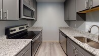 Located at 240 Conant St in Beverly, Massachusetts, this single-floor residential unit offers a well-organized layout with modern finishes throughout. The living area features smooth gray wood-look flooring and large sliding glass doors that invite natural light and provide outdoor views. Adjacent to the living space, the galley-style kitchen is outfitted with sleek gray cabinetry, granite countertops, and stainless steel appliances including a range, microwave, and dishwasher — combining both style and functionality. The bedrooms are finished with plush wall-to-wall carpeting and soft blue-gray painted walls, lending a calm and neutral ambiance. One bedroom includes a double-door closet for generous storage, while another benefits from direct access to a full bathroom. The bathrooms are finished with tile flooring; one features a tub-shower combination with a granite-topped vanity, while another includes a standalone walk-in shower. Throughout the unit, six-panel white doors and clean white trim provide a crisp, cohesive aesthetic. The thoughtfully designed floor plan ensures a comfortable and functional living experience in this Beverly, MA residence.