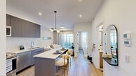 Located at 1750 4 St NE in Calgary, this thoughtfully designed one-bedroom, one-bathroom unit offers a modern living experience with efficient use of space across a single floor. The open-concept kitchen and living area form the heart of the unit, featuring flat-front cabinetry in a warm grey tone, stainless steel appliances including a full-size refrigerator and electric range, a white subway tile backsplash, and a central island with a quartz countertop and bar seating — ideal for casual dining. Light hardwood flooring flows throughout, enhancing the bright, airy feel. The living room is anchored by a sliding glass door that opens onto a private balcony, filling the space with natural light and offering open outdoor views. A wall-mounted mini-split unit provides climate control. The bedroom is a serene retreat, highlighted by a textured feature wallpaper, a built-in closet with sliding doors, and a window overlooking the balcony. The bathroom is clean and contemporary, finished with light wood cabinetry, a white countertop vanity, and light hardwood-style flooring. A welcoming hallway connects the rooms with ease. The overall aesthetic is cohesive and modern, with a neutral palette that creates a calm, livable atmosphere throughout.