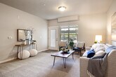 This 1-bedroom, 1-bathroom residence offers a smart, functional layout that maximizes every square foot across a single floor. The open-concept living area serves as the heart of the home, combining the living room, dining area, and kitchen into one cohesive space. The living room features a mix of carpet and hardwood-style flooring, neutral warm-toned walls, and a textured ceiling, with a door providing access to the outdoors and a window that invites natural light. The kitchen is equipped with dark espresso cabinetry reaching to the ceiling, black appliances including a refrigerator and range, a tile backsplash, and granite-style countertops. A breakfast bar with seating connects the kitchen to the dining area, which is accented by a chandelier overhead. The bedroom is a comfortable retreat with carpeted flooring and a walk-in closet outfitted with a hanging rod and built-in shelving. The bathroom features a dark vanity with a granite-style countertop and a large mirror. A dedicated laundry area houses a stacked front-loading washer and dryer alongside an open shelving nook, adding everyday convenience to this well-rounded residence.