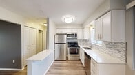 Located at 11201 E 14 Mile Rd in Sterling Heights, Michigan, this thoughtfully updated one-bedroom, one-bathroom unit offers a clean, modern aesthetic throughout. Luxury vinyl plank flooring flows seamlessly across the entire floor plan, complementing the neutral gray and white color palette.

The open-concept kitchen and dining area is a standout feature, showcasing white shaker cabinetry, a mosaic tile backsplash, gleaming white quartz countertops, and a full suite of stainless steel appliances including a refrigerator, range, microwave, and dishwasher. A peninsula counter provides additional prep space and a natural division between the kitchen and dining area.

The living room is generously proportioned, bathed in natural light from large windows and a sliding glass door that opens onto a private balcony with outdoor views. A ceiling fan adds comfort to the space.

The bedroom is a comfortable size, featuring a wide window with views of the surrounding trees and two closets for ample storage. The full bathroom impresses with a dual-sink vanity topped with granite-style countertops, a large mirror, and a tub-shower combination. Additional conveniences include a dedicated laundry area and a hallway connecting all rooms efficiently.