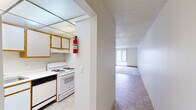 Located at 5900 Bridge Rd in Ypsilanti, Michigan, this two-bedroom, one-bathroom unit offers a practical and comfortable single-floor layout. The kitchen features wood-trimmed cabinetry, white appliances including a gas range and refrigerator, and tile flooring, with a textured drop ceiling adding character to the space. A hallway connects the kitchen to the open living and dining area, which is finished with a combination of tile and carpet flooring and topped with a ceiling fan with light fixture. Large sliding glass doors dressed with vertical blinds allow generous natural light and offer views of the surrounding greenery. The spacious primary bedroom includes a wood-panel sliding closet door and a large window with outdoor views, while the second bedroom features neutral carpet and clean white walls. Both bedrooms are well-proportioned and offer comfortable living space. The bathroom is equipped with a wide vanity countertop, warm wood cabinetry, a mirrored medicine cabinet with overhead lighting, and tile flooring. Two hallways provide functional circulation throughout the unit, and a dedicated closet adds convenient storage. The layout is efficient and well-connected, making the most of the available footprint.