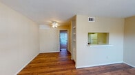 Located at 7000 Greenbriar Dr in Houston's Texas Medical Center area, this single-floor unit offers a practical and comfortable layout throughout. The open living area is finished with warm hardwood-style flooring and features a ceiling fan overhead, creating a bright and airy atmosphere. A half-wall with built-in shelving separates the living space from the kitchen, which includes a pass-through counter for added connectivity. The galley-style kitchen is well-equipped with warm wood cabinetry, white appliances including an electric range, dishwasher, and refrigerator, all set above matching hardwood-style floors. The bedrooms are carpeted for comfort, each outfitted with a ceiling fan and walk-in closet. One bedroom features a sliding glass door with vertical blinds that allows natural light to fill the room and provides outdoor access. Additional rooms with hardwood-style flooring offer flexibility for use as a den, office, or dining space, with large windows inviting ample natural light. The bathroom includes a full tub-shower combo with white tile surround. Throughout the unit, neutral wall tones and clean finishes create a cohesive and move-in ready environment.