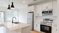 This well-appointed one-bedroom, one-bathroom residence offers a smart, efficient layout with modern finishes and a clean, contemporary aesthetic. The open-concept kitchen serves as the centerpiece of the living space, featuring white shaker cabinetry with matte black hardware, a large island with a white quartz countertop and undermount sink, stainless steel appliances including a refrigerator, electric range, and microwave, and a classic white subway tile backsplash. Warm-toned hardwood flooring flows throughout the main living areas, complemented by recessed lighting and stylish pendant lights above the island. Natural light fills the space through windows dressed with horizontal blinds. The bedroom offers a comfortable footprint with plush carpet flooring, dual windows, a ceiling fan with light fixture, and access to a dedicated closet. The bathroom is finished with wood-look flooring, a white vanity with quartz countertop and matte black fixtures, a glass-enclosed shower, and a walk-in closet conveniently accessible from the bathroom. The overall ambiance is bright, clean, and modern, making efficient use of every square foot.