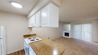 This single-floor residence offers a functional and comfortable layout designed for everyday living. The kitchen serves as a central highlight, featuring white cabinetry, granite-style countertops with a curved breakfast bar peninsula, a white electric range, dishwasher, and full-size refrigerator. Durable wood-look flooring runs throughout the kitchen, which flows seamlessly into the adjacent living area. The living room is generously sized, carpeted for comfort, and anchored by a corner fireplace with a built-in display niche above — a standout architectural detail. Vertical blinds on a large sliding glass door fill the space with natural light while offering privacy. The bedroom is well-proportioned, also featuring soft carpet, a window with vertical blinds, and a baseboard heater. A closet is accessible from the bedroom area, and the hallway connects the rooms with ease. Textured ceilings are present throughout, adding a classic residential character. Neutral warm tones on the walls and flooring create a cohesive, understated palette. The space is clean, move-in ready, and well-suited for those seeking a straightforward, comfortable single-level home.