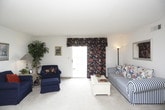 This single-floor residence offers a functional and comfortable layout across several well-defined living spaces. The open living and dining area forms the heart of the home, where neutral carpet and light-toned walls create a bright, welcoming atmosphere. A ceiling fan overhead serves the dining area, which accommodates a wood dining table and chairs. The living area provides ample room for seating and benefits from a sliding glass door that introduces natural light. Framed artwork adorns the walls throughout, adding a personal touch to the space.

The galley-style kitchen is efficiently organized, featuring wood-toned cabinetry, white appliances including a full-size refrigerator, and light countertops along both sides. A wall-mounted intercom adds a practical detail. The kitchen opens directly toward the dining area, supporting easy flow between spaces.

The primary bedroom is generously sized with plush carpet, a window with valance treatments, and direct access to an adjoining room. Additional bedrooms are comfortably proportioned, each with carpet flooring, closet storage, and windows providing natural light. The full bathroom includes a tub and shower combination enclosed by sliding glass doors, a single-sink vanity with wood cabinetry, and tile flooring.