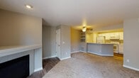This single-floor residence offers a practical and well-organized layout designed for comfortable everyday living. The open-concept living area is a central feature, finished with neutral-toned carpet and complemented by a ceiling fan overhead. A built-in shelving unit provides convenient display or storage space, while a decorative fireplace surround adds a subtle architectural detail to one wall. The transition between the entryway and living area is marked by wood-style flooring, which extends into the kitchen and bathrooms.

The kitchen is separated from the living space by a curved breakfast bar counter, creating a functional divide while maintaining an open feel. White cabinetry lines the walls, offering ample storage, and the kitchen is fully equipped with white appliances including a refrigerator, electric range, microwave, and dishwasher. Wood-style flooring runs throughout the kitchen, lending a clean, cohesive appearance.

The bedrooms are carpeted and well-proportioned, each featuring a ceiling fan and bifold closet doors concealing a rod-and-shelf storage system. Natural light enters through a large window in one bedroom, offering a view of the surrounding outdoor environment. The bathrooms are finished with wood-style flooring, white vanity cabinetry, and chrome fixtures, presenting a clean and functional design throughout.