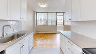 Located at 1209 Richmond St in London, Ontario, this well-appointed one-bedroom, one-bathroom unit offers a practical and comfortable layout across a single floor. The galley-style kitchen is outfitted with white shaker cabinetry, grey countertops, a subway tile backsplash, a stainless steel sink, and a full suite of stainless steel appliances including a range, microwave, and refrigerator. Light tile flooring keeps the kitchen feeling clean and bright. The kitchen opens toward the living area, which showcases classic parquet hardwood flooring that extends throughout the main living spaces and bedroom. Large windows fitted with vertical blinds allow generous natural light to fill the living room, which also features an in-unit air conditioning unit and baseboard heating. The bedroom is a comfortable size, featuring the same warm parquet flooring, access to a dedicated closet, and additional natural light from large windows with urban views. The full bathroom includes a soaking tub with tiled surround, a toilet, and a vanity with stone-look countertops and white cabinetry. Clean white walls and neutral finishes throughout lend the unit a bright, cohesive aesthetic well-suited for everyday living.