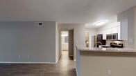 This single-floor residence offers a well-organized layout designed for comfortable everyday living. The open-concept living and dining area features wood-look laminate flooring in a warm medium-brown tone, neutral gray walls, and a textured ceiling throughout. A paneled entry door leads into a generously sized living space that flows seamlessly toward the kitchen peninsula, creating a connected and functional common area.

The kitchen is well-appointed with white shaker-style cabinetry, granite-look countertops, and stainless steel appliances including a range, microwave, and refrigerator. A peninsula with a built-in sink and breakfast bar provides additional workspace and separates the kitchen from the living area.

The bedroom features wood-look flooring, a ceiling fan with light fixture, and a window with blinds allowing natural light. It connects directly to a full bathroom equipped with white cabinetry, granite-look countertops, a single vanity sink, a tub/shower combination with tiled surround, and a wall-mounted vanity light. A separate utility area accommodates laundry hookups. The overall ambiance is clean, modern, and move-in ready.