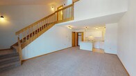This two-story residence offers a thoughtfully designed layout that maximizes space and natural light throughout. The main level opens into a generous living area with plush carpeting and a striking open staircase crafted from warm-toned wood, which leads to the upper floor. The kitchen is efficiently arranged with white cabinetry, light countertops, a full suite of white appliances including a range, dishwasher, and refrigerator, and durable light wood laminate flooring. A kitchen island adds additional workspace and visual separation from the living area.

Ascending the staircase, the upper level reveals a spacious loft-style area bathed in natural light from dual skylights set into the vaulted ceiling, complemented by a ceiling fan. An open railing along the landing maintains a sense of connectivity between floors. The bedroom features soft carpeting, a ceiling fan, and a dedicated closet. The full bathroom is clean and well-appointed, offering a single-sink vanity with white cabinetry, a large mirror, tile flooring, and a full tub-shower combination. A sliding glass door on the upper level provides access to an outdoor area, allowing natural light to fill the space. Throughout, warm wood trim and white walls create a bright, welcoming atmosphere.