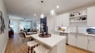 Located at 12231 Pioneers Way in Orlando, FL, this single-floor residence offers a thoughtfully designed open-concept layout that seamlessly connects the kitchen, dining, and living areas. The kitchen is a standout feature, showcasing crisp white shaker cabinetry, open shelving, a classic subway tile backsplash, quartz countertops, a central island with pendant lighting, and a full suite of stainless steel appliances. Light wood-tone flooring runs throughout, enhancing the bright and airy atmosphere created by recessed lighting and natural light from large windows. The living area is generously proportioned, anchored by a ceiling fan and complemented by a bold dark accent wall that adds depth and contemporary contrast. The bedroom is a calm retreat, featuring large windows with sheer curtains that allow ample natural light, light wood flooring, and a comfortable, well-scaled layout. The bathroom is finished with white cabinetry, quartz countertops, a wide vanity mirror, and a full tub-shower combination, maintaining the clean and modern aesthetic found throughout the residence. Overall, the space presents a cohesive, modern design with neutral tones, quality finishes, and a functional flow suited for contemporary living.