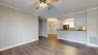 This single-floor space offers a thoughtfully designed layout with a seamless flow between the main living areas. The open-concept living and dining area is finished with rich, dark hardwood-style flooring and features crown molding along the ceilings, adding a clean, polished look. A ceiling fan with a light fixture provides both airflow and illumination, while a door with sidelights allows natural light to filter in, brightening the space. The kitchen is positioned adjacent to the dining area, separated by a raised peninsula counter finished with a dark countertop. White cabinetry provides ample storage, and stainless steel appliances, including a refrigerator and range, complete the functional cooking space. A pendant light fixture above the dining area adds a refined touch. The bedrooms are carpeted for comfort, each equipped with a ceiling fan and natural light from windows with blinds. The bathroom is cleanly finished with a white vanity, full tub-shower combination, and coordinating hardwood-style flooring, maintaining the consistent, neutral aesthetic found throughout the unit. Overall, the space presents a balanced combination of practical layout and modern, understated finishes.