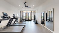 Located at 1004 Via Corso Ave in Mauldin, SC, this fitness center is a thoughtfully designed exercise space that blends modern functionality with attractive architectural details. The room features durable speckled rubber flooring throughout, providing a practical and resilient surface suited for a variety of workout activities.

The space is equipped with multiple treadmills, an elliptical trainer, a stationary spin bike, a cable resistance machine, and an adjustable weight bench, offering a comprehensive range of cardio and strength training options. Full-length mirrors are mounted along one wall, enhancing the sense of openness while allowing users to monitor their form during exercise.

A striking wall of black-framed floor-to-ceiling glass doors floods the interior with natural light and provides direct access to an adjoining outdoor patio. The patio features exposed brick walls, a decorative egg chair with an ottoman, and potted greenery, creating a relaxed retreat area just steps from the gym floor. Recessed ceiling lighting and a large ceiling fan ensure comfortable air circulation and well-distributed illumination throughout the interior.

The white walls contrast cleanly with the dark door frames and equipment, giving the space a crisp, contemporary aesthetic. A wall-mounted split air conditioning unit adds climate control convenience. Overall, this fitness center delivers a polished, fully functional environment for a well-rounded exercise routine.