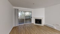 Located at 600 7th Avenue in Seattle, WA, this two-bedroom, two-bathroom residence offers a well-designed single-floor layout with a clean, modern aesthetic. The living room serves as the heart of the home, featuring warm hardwood-style flooring, a tile-surround fireplace, and sliding glass doors that open to an outdoor balcony, filling the space with natural light and views of surrounding greenery. The kitchen is designed for functionality, boasting white cabinetry, dark countertops, a peninsula with a built-in sink, and white appliances including a range and refrigerator. A hallway connects the main living areas to the two bedrooms, both of which are carpeted for comfort. The primary bedroom offers ample square footage with a ceiling fan, dual windows, and generous closet space with built-in shelving. The second bedroom also features carpet and a reach-in closet. Both bathrooms are finished with hardwood-style flooring, tub-shower combinations, and clean white fixtures. A dedicated in-unit laundry area with a washer and overhead shelving adds everyday convenience. The overall design is bright and neutral throughout, making for a practical and comfortable living environment in the heart of Seattle.