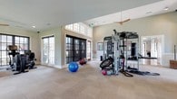 The fitness center at Greystone At Oakland is a thoughtfully designed, single-floor amenity space that combines elegant architectural details with a comprehensive range of workout facilities. The entry lobby sets a refined tone with soaring ceilings, white decorative columns, wainscoting, hardwood-style flooring, and a statement globe chandelier. Large multi-pane glass doors flood the space with natural light, while a seating area provides a welcoming transition into the fitness areas beyond.

The main workout floor is expansive and open, featuring neutral carpet tile flooring and elevated ceilings with ceiling fans for air circulation. This central zone houses a Life Fitness Synergy multi-functional cable machine, balance and stability equipment including exercise balls, battle ropes, and a balance board, making it well-suited for functional and cross-training workouts.

A dedicated cardio room offers multiple treadmills and an elliptical machine, all positioned in front of large windows overlooking the outdoors. A separate strength training room provides a full rack of dumbbells, a weight bench, and a squat rack with barbell, supported by natural light from oversized windows.

Completing the amenity space is a compact, well-organized laundry room equipped with front-loading washers and dryers, a folding counter, built-in cabinetry, and a community bulletin board.