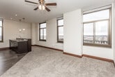 This single-floor urban residence offers a thoughtfully designed open-concept layout, filled with natural light from an abundance of large, dark-framed windows that frame impressive views of the surrounding cityscape and waterfront. The expansive living and dining area features plush carpeting, rich dark wood baseboards, and a ceiling fan with integrated lighting, creating a comfortable and inviting atmosphere.

The kitchen is a standout feature, equipped with dark espresso cabinetry, granite countertops, and a full suite of black appliances including a range, microwave, and refrigerator. A peninsula with a built-in sink and pendant lighting above seamlessly connects the kitchen to the main living space, making it ideal for both everyday living and entertaining.

The bedroom is generously sized, flooded with natural light through multiple large windows that offer elevated views of neighboring buildings and the city beyond. Ceiling fans in both the bedroom and living areas ensure year-round comfort.

The bathroom is finished with a modern dark vanity, vessel sink, neutral countertops, and wood-look tile flooring. Ample storage cabinetry adds practical functionality. Tile flooring in the entry and kitchen transitions to soft carpet in the living and sleeping areas, tying the space together with a warm, cohesive aesthetic throughout.