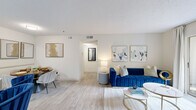 This thoughtfully designed one-bedroom, one-bathroom residence offers a comfortable and efficient layout across a single floor. Light wood-look flooring flows throughout, complementing the bright, neutral palette that defines each room.

The open-concept living and dining area forms the heart of the home, bathed in natural light from large windows and a sliding glass door that opens to a private balcony overlooking greenery. The living space provides ample room for seating and entertaining, while the adjacent dining area accommodates a full dining set with ease.

The kitchen is outfitted with crisp white upper cabinetry, rich dark lower cabinets, light quartz countertops, and stainless steel appliances including a dishwasher, range, and microwave — a clean, contemporary design that balances style and function.

The bedroom is a serene retreat, featuring a ceiling fan, a large window with verdant views, and direct access to the in-unit laundry area, which houses a full-size washer and dryer with overhead shelving for added storage.

The bathroom is finished in clean whites with a shower-tub combination. Throughout the residence, a textured ceiling, recessed lighting, and consistent flooring tie the spaces together into a cohesive, welcoming home.