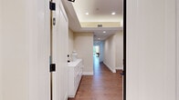 Located at 1823 Pandora Ave in Los Angeles, this refined two-story home offers four bedrooms and four bathrooms across a generously proportioned layout. The main floor impresses with an expansive living and dining area showcasing a striking coffered ceiling with recessed lighting, rich hardwood floors, and large windows that invite abundant natural light. The gourmet kitchen is appointed with dark wood cabinetry, dramatic marble-veined stone countertops and backsplash, and a classic tile floor, combining style with functionality. A sweeping staircase with ornate wrought iron railings and an elegant crystal chandelier serves as a grand focal point connecting both levels. The upper floor hosts well-appointed bedrooms, including a spacious primary suite with tray ceiling accents and a dedicated walk-in closet featuring cedar-paneled wardrobes and custom built-in shelving. Bedrooms offer hardwood flooring, tray ceilings, and large windows with views to the exterior. The bathrooms are thoughtfully finished — one features warm beige tile with a frameless glass shower enclosure, while another offers grey stone tile, a rainfall showerhead, and a smart toilet. Wide hallways with recessed lighting and clean white millwork connect each space seamlessly throughout both floors.