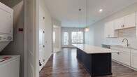 Located at 1145 Chambers Rd in Columbus, Ohio, this single-floor space offers a thoughtfully designed open layout with contemporary finishes throughout. The kitchen serves as a central highlight, featuring a large dark-base island topped with a white quartz countertop with subtle veining, providing ample prep and gathering space. White shaker-style cabinetry lines the walls, complemented by a classic subway tile backsplash and a full suite of stainless steel appliances, including a French door refrigerator, electric range, built-in microwave, and dishwasher. Globe pendant lights with brass accents hang above the island, adding warmth to the clean aesthetic. Rich, dark hardwood-style flooring runs through the main living and kitchen areas, grounding the neutral color palette of soft gray and white walls. The living area connects seamlessly to the kitchen and receives natural light through a glass-paned exterior door. The bedroom is carpeted in neutral tones and features a window with outdoor views. The bathroom includes a dark-cabinetry vanity with a white countertop, wood-look flooring, and direct access to a walk-in closet with built-in shelving, offering practical storage solutions throughout.