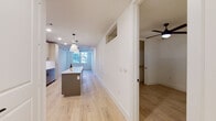 This thoughtfully designed single-floor residence showcases a clean, contemporary aesthetic with light hardwood flooring flowing seamlessly throughout the main living areas. The open-concept layout centers around a well-appointed kitchen featuring a large central island with a white quartz countertop, pendant lighting, light wood upper cabinetry with glass accents, and a full suite of stainless steel appliances including a gas range, built-in microwave, dishwasher, and side-by-side refrigerator. A classic white subway tile backsplash completes the kitchen's modern look. The expansive living area extends the full length of the space, bathed in natural light from large windows, and is finished with a ceiling fan overhead. The primary bathroom is a standout feature, offering a double-sink vanity with dark cabinetry and matte black fixtures, large-format tile flooring, and a soaking tub fully surrounded by dramatic marble-style tile. A second full bathroom mirrors the same refined finishes. A dedicated in-unit laundry room provides added convenience. The bedroom is generously sized, featuring natural light, a ceiling fan, and a walk-in closet. Crisp white walls, recessed lighting, and consistent finishes throughout create a bright, cohesive, and move-in-ready living environment.