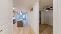 This thoughtfully designed single-floor residence showcases a clean, contemporary aesthetic with light hardwood flooring flowing seamlessly throughout the main living areas. The open-concept layout centers around a well-appointed kitchen featuring a large central island with a white quartz countertop, pendant lighting, light wood upper cabinetry with glass accents, and a full suite of stainless steel appliances including a gas range, built-in microwave, dishwasher, and side-by-side refrigerator. A classic white subway tile backsplash completes the kitchen's modern look. The expansive living area extends the full length of the space, bathed in natural light from large windows, and is finished with a ceiling fan overhead. The primary bathroom is a standout feature, offering a double-sink vanity with dark cabinetry and matte black fixtures, large-format tile flooring, and a soaking tub fully surrounded by dramatic marble-style tile. A second full bathroom mirrors the same refined finishes. A dedicated in-unit laundry room provides added convenience. The bedroom is generously sized, featuring natural light, a ceiling fan, and a walk-in closet. Crisp white walls, recessed lighting, and consistent finishes throughout create a bright, cohesive, and move-in-ready living environment.