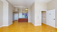 This single-floor unit is characterized by warm hardwood flooring that flows consistently throughout, creating a cohesive and inviting aesthetic across all areas. The open-concept layout connects the living area to the kitchen, which serves as a functional centerpiece of the space. The kitchen is well-appointed with rich wood cabinetry, a granite-topped peninsula with an undermount sink, and a full suite of stainless steel appliances including a refrigerator, range, and built-in microwave. A pendant chandelier above the peninsula adds a refined touch to the cooking and dining area.

The living area is generously proportioned with neutral-toned walls and a clean, open feel. Adjacent spaces include two versatile rooms, each featuring hardwood floors, neutral walls, and windows fitted with horizontal blinds that allow for controlled natural light. One room benefits from a pair of windows that bring in ample daylight and offer views of the surrounding area.

The bathroom is efficiently designed, featuring a glass-enclosed shower stall, hardwood flooring, and oil-rubbed bronze hardware accents including hooks and towel bars that add a polished, cohesive detail. An open closet space with a rod is also present, providing convenient storage. Overall, the unit maintains a clean, modern character throughout.