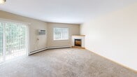 Located at 24905 CR-75 in St. Augusta, Minnesota, this 2-bedroom, 1-bathroom single-floor unit offers a practical and comfortable layout. The combined kitchen and living room forms the heart of the space. The living room features soft carpeting, a corner electric fireplace with a wood-trimmed surround, a large window that fills the room with natural light, and a wall-mounted air conditioning unit alongside baseboard heating. The kitchen is equipped with oak cabinetry, dark laminate countertops, tile flooring, and white appliances including a refrigerator, dishwasher, range, and microwave. A carpeted hallway connects the living areas to the two bedrooms, both of which feature neutral-toned walls, plush carpet, baseboard heating, and windows overlooking the surrounding greenery. The primary bedroom includes access to a walk-in closet outfitted with wire shelving and hanging rods on two walls, providing generous storage. The full bathroom features tile flooring, a tub-shower combination, a toilet, and a vanity with a marble-patterned countertop. Throughout the unit, light wood trim accents doorways and baseboards, contributing to a clean, cohesive aesthetic.