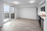 Located at 18 Tretti Way in Toronto's north end, this two-bedroom, one-bathroom unit offers a efficiently designed single-floor layout with a clean, contemporary aesthetic throughout. Light wood laminate flooring runs continuously across all rooms, complementing the bright white walls and ceilings to create a fresh, airy atmosphere.

The living area is bathed in natural light through large floor-to-ceiling sliding glass doors that open to a balcony, offering open views of the surrounding cityscape. The space is well-lit with modern flush-mount ceiling fixtures. A stainless steel refrigerator is visible near the living area, indicating a practical kitchen layout.

The primary bedroom features its own sliding glass balcony door, allowing for additional natural light and outdoor access, while the second bedroom includes a large window framing city views. Both bedrooms feature the same warm wood flooring and neutral white walls, providing a versatile canvas for personalization. A connecting hallway with a sliding closet door links the rooms efficiently.

The bathroom is finished with crisp white subway-tiled walls and includes a glass-enclosed walk-in shower with a rain showerhead and brushed nickel fixtures, conveying a sleek, modern design. Overall, the unit presents a bright, minimalist living environment well-suited for urban living in Toronto.