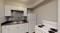 Located at 1440–1491 W Rich St in Columbus, Ohio, this single-floor unit offers a well-organized layout with a clean, updated aesthetic throughout. The open living area features light wood-style luxury vinyl flooring that extends seamlessly through the main spaces, creating a cohesive and modern feel. Wall sconce lighting and a neutral gray-and-white color palette give the interior a bright, welcoming ambiance.

The kitchen is thoughtfully appointed with white shaker-style cabinetry, dark countertops, a stainless steel double-basin sink, and a striking mosaic tile backsplash in varying shades of gray. White appliances, including a refrigerator and electric range, complete the functional cooking space.

The bedrooms are comfortably sized, each featuring large windows that allow natural light to filter in, along with ceiling fans for added comfort. Built-in closets provide convenient storage. The full bathroom is finished in a clean, all-white scheme, featuring a tub-shower combination, a white vanity, and wood-look tile flooring.

The entry area includes wall-mounted lighting and an electrical panel, adding to the unit's practical design. Overall, this space presents a neat, move-in-ready environment with modern updates and a straightforward, functional floor plan suited for everyday living.