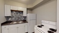 Located at 1440–1491 W Rich St in Columbus, Ohio, this single-floor unit offers a well-organized layout with a clean, updated aesthetic throughout. The open living area features light wood-style luxury vinyl flooring that extends seamlessly through the main spaces, creating a cohesive and modern feel. Wall sconce lighting and a neutral gray-and-white color palette give the interior a bright, welcoming ambiance.

The kitchen is thoughtfully appointed with white shaker-style cabinetry, dark countertops, a stainless steel double-basin sink, and a striking mosaic tile backsplash in varying shades of gray. White appliances, including a refrigerator and electric range, complete the functional cooking space.

The bedrooms are comfortably sized, each featuring large windows that allow natural light to filter in, along with ceiling fans for added comfort. Built-in closets provide convenient storage. The full bathroom is finished in a clean, all-white scheme, featuring a tub-shower combination, a white vanity, and wood-look tile flooring.

The entry area includes wall-mounted lighting and an electrical panel, adding to the unit's practical design. Overall, this space presents a neat, move-in-ready environment with modern updates and a straightforward, functional floor plan suited for everyday living.