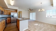 Located on Berthoud Parkway in Loveland, CO, this single-floor unit offers a thoughtfully designed open-concept layout that seamlessly connects the kitchen, dining, and living areas. The kitchen is a standout feature, showcasing warm knotty-pine cabinetry, dark granite-style countertops, and a full suite of stainless steel appliances including a side-by-side refrigerator with ice maker, an electric range, and an over-the-range microwave. A central island with a double sink and built-in seating overhang provides both additional prep space and a casual dining option. Durable wood-look flooring runs throughout the kitchen, transitioning to plush neutral carpet in the living and bedroom areas. The living space is well-lit by a sliding glass door with vertical blinds, allowing natural light to filter through, and is accented by a ceiling fan and an elegant chandelier. The bedroom is a comfortable, carpeted retreat featuring its own ceiling fan and a bright window with blinds offering views of the surrounding area. The bathroom is clean and functional, with a full tub-shower combination, wood-look flooring, and classic white fixtures. Overall, the unit presents a practical and inviting atmosphere well-suited for comfortable everyday living.