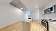 Located at 1020 De Bleury in the heart of Montréal, this well-appointed 2-bedroom, 2-bathroom unit offers a thoughtfully designed layout across a single floor. The open-concept living and kitchen area serves as the centerpiece of the space, featuring warm light hardwood flooring, crisp white walls, and striking exposed concrete ceiling panels that lend an industrial-modern character. The kitchen is equipped with stainless steel appliances, white cabinetry with a subway tile backsplash, and a central island with a built-in sink and a gold-tone faucet — ideal for both meal preparation and casual dining. Track lighting illuminates the kitchen, while the living area benefits from natural light through large windows overlooking the surrounding cityscape. Both bedrooms are well-proportioned, continuing the hardwood flooring and clean aesthetic, each supported by dedicated closet space. The two bathrooms are finished with neutral tile, modern square-basin vanities, framed mirrors, and glass-enclosed showers. A convenient in-unit laundry area includes a stacked washer and dryer alongside built-in wire shelving for storage. A hallway connects the rooms efficiently, completing this clean, contemporary urban residence.