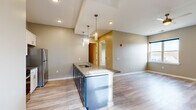 Located at 5050 Transit Rd in Depew, NY, this thoughtfully designed single-floor unit offers a comfortable and modern living experience across six rooms. The open-concept kitchen and living area serves as the heart of the space, anchored by a striking kitchen island with granite countertops, navy blue cabinetry, and an integrated sink. Elegant pendant lighting hangs above the island, complementing the recessed ceiling lights throughout. Stainless steel appliances, including a full-size refrigerator, complete the kitchen, which also features white upper cabinetry with brushed nickel hardware. Light-toned luxury vinyl plank flooring flows through the main living areas, providing a clean, contemporary aesthetic. The bedrooms offer plush carpeting and large windows that fill each room with natural light and offer views of the surrounding neighborhood. Neutral, warm-toned walls throughout create a cohesive and inviting ambiance. The bathroom is well-appointed with white cabinetry, a vanity with granite countertop, and wood-look tile flooring. A dedicated utility area houses a stacked washer and dryer unit, adding everyday convenience. The layout is efficient and well-organized, making excellent use of the available space.