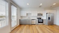 Located at 5750 Airport Rd in Santa Fe, New Mexico, this efficiently designed one-bedroom, one-bathroom unit offers a thoughtful layout across a single floor. Light wood-look flooring flows throughout the main living areas, creating a clean and cohesive aesthetic.

The kitchen is a standout feature, showcasing two-tone cabinetry with white upper cabinets and gray lower cabinets, complemented by a marble-style tile backsplash and white quartz countertops. A full suite of stainless steel appliances—including a refrigerator with ice maker, electric range, built-in microwave, and dishwasher—provides modern functionality. Large windows with horizontal blinds allow ample natural light into the space.

A bright hallway connects the rooms, lined with recessed lighting and a smart thermostat on the wall. The bedroom features soft carpeting underfoot, a ceiling fan, and a high clerestory window that brings in additional natural light. A dedicated closet provides convenient storage.

The bathroom is finished in the same contemporary palette, featuring gray cabinetry with a white countertop vanity, a large mirror, and a tiled walk-in shower with a glass enclosure. Light wood-look flooring continues here, maintaining consistency throughout the unit.

Overall, the space presents a clean, modern, and move-in-ready environment with quality finishes throughout.