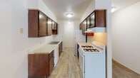 Located at 2525 Williams Dr in Burnsville, Minnesota, this single-floor unit offers a functional and practical layout across several well-defined living spaces. The galley-style kitchen is equipped with dark wood cabinetry lining both walls, a gas range, refrigerator, dishwasher, and a built-in sink with ample counter space. Light wood-style flooring runs through the kitchen, providing a clean contrast to the warm-toned cabinetry. The living area features plush carpeting, a ceiling fan, and an open sightline to the kitchen, creating a connected and easy-to-navigate floor plan. Bedrooms are carpeted and generously sized, each featuring large windows dressed with vertical blinds that allow natural light to fill the rooms. Baseboard heating runs along the perimeter of the bedroom walls, and at least one bedroom includes a wall-mounted air conditioning unit and a spacious closet with built-in shelving. The bathrooms include a combined tub and shower with white surround, as well as a separate stall shower with a glass enclosure, both featuring wood-toned vanities with single-sink countertops and well-lit mirrors. Textured ceilings are consistent throughout the unit, contributing to a classic residential aesthetic.