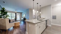 Located in Charlotte, NC, this thoughtfully designed one-bedroom, one-bathroom residence offers a functional and stylish open-concept layout across a single floor. The kitchen and living area flow seamlessly together, anchored by a standout granite-topped island with a black matte sink fixture and pendant lighting overhead. White shaker-style cabinetry, stainless steel appliances, and light hardwood-style flooring give the kitchen a clean, modern aesthetic. The adjacent living room features rich dark hardwood-style flooring, a bold teal accent wall, large windows, and a glass door that invites natural light and outdoor views, creating a bright and welcoming atmosphere. The bedroom is a comfortable retreat with soft neutral tones and ample space for a full furniture arrangement. A dedicated walk-in closet with wire shelving and plush carpet provides generous storage. The bathroom is finished with light wood-tone vanity cabinetry, a wide mirror, white countertops, and a full tub-shower combination with large-format tile surround. Hardwood-style flooring carries through the bathroom, tying the home together with a cohesive design. Overall, this residence combines contemporary finishes with a warm, livable ambiance.