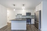 Located at 4981 Bathurst St in North York, Toronto, this well-appointed one-bedroom, one-bathroom unit offers a thoughtfully designed layout across a single floor. The open-concept kitchen and living area serves as the heart of the space, showcasing crisp white shaker cabinetry, a light grey subway tile backsplash, and dark countertops that provide a striking contrast. A central kitchen island offers additional prep and dining space, while pendant lighting adds a modern, polished touch. Stainless steel appliances — including a refrigerator, range, microwave, and dishwasher — complete the kitchen's contemporary feel. Warm hardwood-style flooring runs throughout, lending a cohesive and inviting character to the entire unit. The bedroom is a serene, light-filled retreat with two windows overlooking greenery, offering pleasant outdoor views and a calm ambiance. A wall-mounted heating unit ensures year-round comfort. The bathroom features classic white subway tile surrounding a full soaker tub and shower combination, accented by chrome fixtures for a clean, timeless finish. Overall, the unit's modern finishes, functional layout, and natural light make it a practical and attractive living space in a convenient Toronto neighbourhood.
