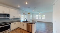 This well-appointed single-floor residence offers a thoughtfully designed open-concept layout that seamlessly connects the kitchen and living areas. The kitchen is a standout feature, showcasing crisp white cabinetry, dark countertops, a subway tile backsplash, and a full suite of stainless steel appliances including a French door refrigerator, electric range, microwave, and dishwasher. A peninsula with pendant lighting serves as both a functional workspace and a natural divider between the kitchen and the generously sized living area. The living space is bathed in natural light through multiple windows fitted with blinds, and is further enhanced by durable hardwood-style flooring and a ceiling fan. French doors provide additional light and outdoor access. The bedrooms are finished with plush carpeting and ceiling fans, offering a comfortable retreat. The primary bedroom connects to a well-lit bathroom featuring a single vanity with dark countertops, a framed mirror, and direct access to a spacious walk-in closet complete with built-in shelving and hanging rods. Throughout the residence, clean white walls, recessed lighting, and consistent finishes create a cohesive, modern aesthetic that is both functional and inviting.