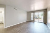This single-story residence offers a thoughtful layout across two bedrooms, two bathrooms, a kitchen, living room, laundry, hallway, and three closets. The living room is a highlight of the home, featuring warm wood-style flooring, neutral gray walls, and a full-width sliding glass door that floods the space with natural light and provides direct access to an outdoor area with views of the surrounding greenery. The galley-style kitchen is outfitted with dark cabinetry, marble-pattern countertops, and black appliances including a range, refrigerator, and built-in microwave, all complemented by light wood-style flooring. The bathrooms echo the kitchen's design with matching dark vanity cabinetry, marble-pattern countertops, and mirrored medicine cabinets. The bedrooms are finished with the same light wood-style flooring and neutral tones; the secondary bedroom features a ceiling fan and a bright window, while the primary bedroom offers generous proportions and direct access to a bathroom. Three closets, including walk-in storage with built-in shelving, provide excellent organizational capacity. The consistent use of light, neutral tones and cohesive finishes throughout gives the home a clean, modern, and welcoming ambiance.