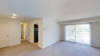 This single-floor residence offers a practical and comfortable layout with neutral finishes throughout. The living area is spacious and carpeted, featuring clean white walls and a large sliding glass door fitted with vertical blinds that frames views of surrounding greenery while allowing natural light to fill the space. An adjacent hallway connects the living area to the rest of the unit, which includes a closeted entry with a bi-fold door.

The kitchen is efficiently designed with rich wood cabinetry, granite-style countertops, and a full suite of stainless steel appliances, including a gas range, over-the-range microwave, refrigerator, and dishwasher. A window above the sink provides natural light and outdoor views.

The bedrooms are carpeted and feature neutral walls, with windows that bring in natural light. Built-in closet space is present, and the rooms offer ample room for furnishings. The bathroom includes a full soaking tub and shower combination with clean cream-toned tile surround and brushed nickel fixtures. Throughout the unit, the overall aesthetic is clean, understated, and move-in ready.
