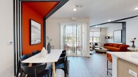 This single-floor residence showcases a striking contemporary design defined by a bold color palette, clean lines, and thoughtful architectural detailing throughout. The open-plan living and dining area serves as the heart of the home, where a vivid orange accent wall and black linear ceiling trim create a dramatic visual contrast against crisp white walls and light wood-style flooring. Large sliding glass doors flood the dining area with natural light and provide direct access to an outdoor space, while the adjacent living room offers additional windows with outdoor views, reinforcing a bright and airy atmosphere.

The kitchen is outfitted with flat-front light wood cabinetry, white quartz countertops, a classic subway tile backsplash, and a suite of stainless steel appliances, combining style with practicality. A breakfast bar adds casual dining versatility.

The bedroom is a serene retreat featuring plush carpet, multiple windows dressed in elegant floor-length curtains, and a distinctive arched accent wall behind the bed. A sliding-door closet provides generous storage. The en-suite bathroom features a long vanity with light wood cabinetry, a glass-enclosed shower with full-height tile surround, and warm wood-look flooring. A separate powder room with a single vanity and wood flooring completes the layout. Throughout, the design maintains a cohesive modern aesthetic with warm tones and curated finishes.