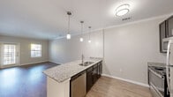 This single-floor residence offers a practical and thoughtfully designed layout, accommodating four bedrooms and three full bathrooms. The open-concept living and kitchen area forms the heart of the home, where rich hardwood-style flooring extends seamlessly beneath crown molding-trimmed ceilings. The kitchen is anchored by a central island featuring granite countertops, a stainless steel sink, and a dishwasher, all illuminated by a trio of pendant lights. Double entry doors and a chandelier in the entryway add an elegant touch to the arrival experience. The living room receives generous natural light through a front-facing door and dual windows, creating a bright and welcoming atmosphere. The bedrooms offer plush carpeting, ceiling fans, and windows that bring in natural light, while the spacious primary bedroom includes a walk-in closet with built-in wire shelving. The three bathrooms are finished with white subway tile surrounds, soaking tubs, and brushed nickel fixtures—one featuring a multi-function shower panel system. Neutral warm-gray tones throughout the walls tie the entire space together in a cohesive, move-in-ready aesthetic.