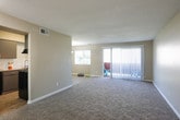 This single-floor residence offers a thoughtfully arranged layout connecting living, dining, kitchen, and bedroom spaces in a cohesive flow. The open-concept living and dining area is generously sized, finished with plush wall-to-wall carpeting and neutral beige walls that create a warm, understated atmosphere. A pendant light fixture anchors the dining space, while a large sliding glass door fitted with vertical blinds opens to an outdoor patio, allowing natural light to fill the room. A standard window further brightens the area.

The kitchen is positioned adjacent to the living space and features gray cabinetry with brushed nickel hardware, granite-look countertops, a white subway tile backsplash, and wood-look vinyl flooring. Black appliances, including a dishwasher, complement the contemporary aesthetic.

The bedrooms are carpeted and well-proportioned. One bedroom includes two closets—one featuring louvered bifold doors—providing ample storage. Additional bedrooms offer window access to natural light and easy connectivity to adjoining rooms.

The bathroom is finished with consistent gray cabinetry, granite countertops, a well-lit vanity mirror, wood-look flooring, and a shower-tub combination. Textured ceilings are present throughout, contributing to the unit's cohesive, move-in-ready character.