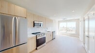 Located at 922 N Broad St in Philadelphia's vibrant North Broad corridor, this modern one-bedroom, one-bathroom residence offers a thoughtfully designed layout across a single floor. Light wood-tone cabinetry lines the open kitchen, which is equipped with a full suite of stainless steel appliances including a refrigerator, electric range, built-in microwave, and dishwasher. A white subway tile backsplash and clean white countertops complete the contemporary aesthetic, while light hardwood-style flooring flows seamlessly into the adjoining living area. A large picture window at the end of the living space frames sweeping views of the Philadelphia skyline, flooding the room with natural light. The bedroom is a calm, neutral retreat featuring its own oversized window with city views and a dedicated closet with sliding doors. An in-unit laundry area adds everyday convenience. The bathroom is finished in crisp white tile with a walk-in shower fitted with a rainfall showerhead and glass panel enclosure, complemented by marble-style flooring. Recessed lighting throughout and a ceiling-mounted HVAC unit ensure comfort year-round. The overall design is clean, minimal, and well-suited for modern urban living.