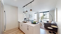 Located at 300 N Michigan Ave in Chicago, this modern residence offers a thoughtfully designed open-concept layout bathed in natural light. The kitchen serves as a centerpiece of the living space, featuring a large white quartz island with an undermount sink, black matte hardware, and sleek white cabinetry extending to the ceiling. Stainless steel appliances — including a full-size refrigerator, gas range, and built-in microwave — complement the contemporary aesthetic, while a trio of pendant lights with mixed glass and metal shades adds a stylish focal point overhead. Light hardwood flooring flows seamlessly throughout, connecting the kitchen to an open dining and living area. The living room is bright and airy, anchored by floor-to-ceiling windows that frame sweeping city views of the Chicago skyline. The space accommodates a comfortable sectional sofa, round coffee tables, and a sculptural arc floor lamp. Two bedrooms continue the clean, modern palette with large windows, light walls, and ample natural light. The primary bedroom features a gallery wall and generous window views of the surrounding high-rises, while the secondary bedroom benefits from a wall of windows and well-organized storage. A bathroom with walk-in shower completes this well-appointed urban residence.