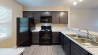 Located at 3002 Kingston Cir in Greenville, NC, this two-floor home offers a thoughtfully laid-out interior with consistent finishes throughout. The main level features an open living area with wood-look flooring, a ceiling fan, and a staircase with white railings leading to the upper floor. The kitchen is well-appointed with dark shaker-style cabinetry, light marble-patterned countertops, and black appliances including a refrigerator, electric range, microwave, and sink — all set against matching wood-look flooring. A bathroom on the main level features a white vanity with ample storage, a large mirror, and a tub-shower combination with clean white surround. Upstairs, the bedrooms feature vaulted ceilings with ceiling fans, wood-look flooring, and windows with blinds that allow natural light and neighborhood views. The warm neutral wall tones carried throughout both floors lend a cohesive, welcoming ambiance. An additional bathroom upstairs mirrors the clean, functional design of the main-level bath, complete with a white vanity and tub-shower unit. The overall aesthetic is clean and move-in ready, with practical finishes suited for comfortable everyday living.