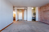 Located at 213 Delaware St in the heart of Kansas City's historic River Market neighborhood, this single-floor loft-style unit blends industrial character with functional modern living. The open main living area is defined by a striking exposed brick accent wall, soft carpeting underfoot, and a track lighting system overhead that provides flexible illumination throughout the space. A structural column with a sliding barn-style door adds an authentic industrial touch, seamlessly connecting the living area to the rest of the unit. The galley kitchen is well-appointed with dark cabinetry, granite-style countertops, and a full suite of black appliances including a refrigerator, dishwasher, electric range, and over-the-range microwave, all set on durable hardwood-style flooring. The bedroom continues the loft aesthetic with exposed brick walls and large windows that invite abundant natural light. The bathroom features wood-look flooring, a vanity with cabinet storage, a medicine cabinet mirror, and updated fixtures. Throughout the unit, the combination of raw brick, neutral tones, and thoughtful finishes creates a warm, urban ambiance consistent with Kansas City's revitalized warehouse district character.