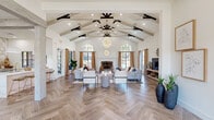 Located at 1909 Hinson Loop Rd in Little Rock, AR, this beautifully designed single-floor space makes a striking first impression with a grand entryway featuring tall wood double doors framed by arched transom and sidelight windows that flood the interior with natural light. Herringbone-patterned wood-look tile flooring flows seamlessly throughout the main areas, anchoring the space with warmth and visual sophistication.

The primary living room is a showstopper, boasting soaring cathedral ceilings with exposed wood beam trusses accented by dark iron detailing, a statement chandelier, and a classic brick fireplace. Arched windows and French doors line the walls, offering abundant outdoor views and light. A second, more intimate living area continues the herringbone flooring with elevated windows and neutral, airy finishes.

The dining room is bright and inviting, highlighted by an arched grid window and curated wall art. A dedicated reception and office area features plush patterned carpeting, a wood-front reception desk with a sliding barn door accent, and a private office with tall grid windows that frame outdoor greenery. Throughout, crisp white walls, natural textures, and carefully chosen furnishings create a cohesive, refined aesthetic.